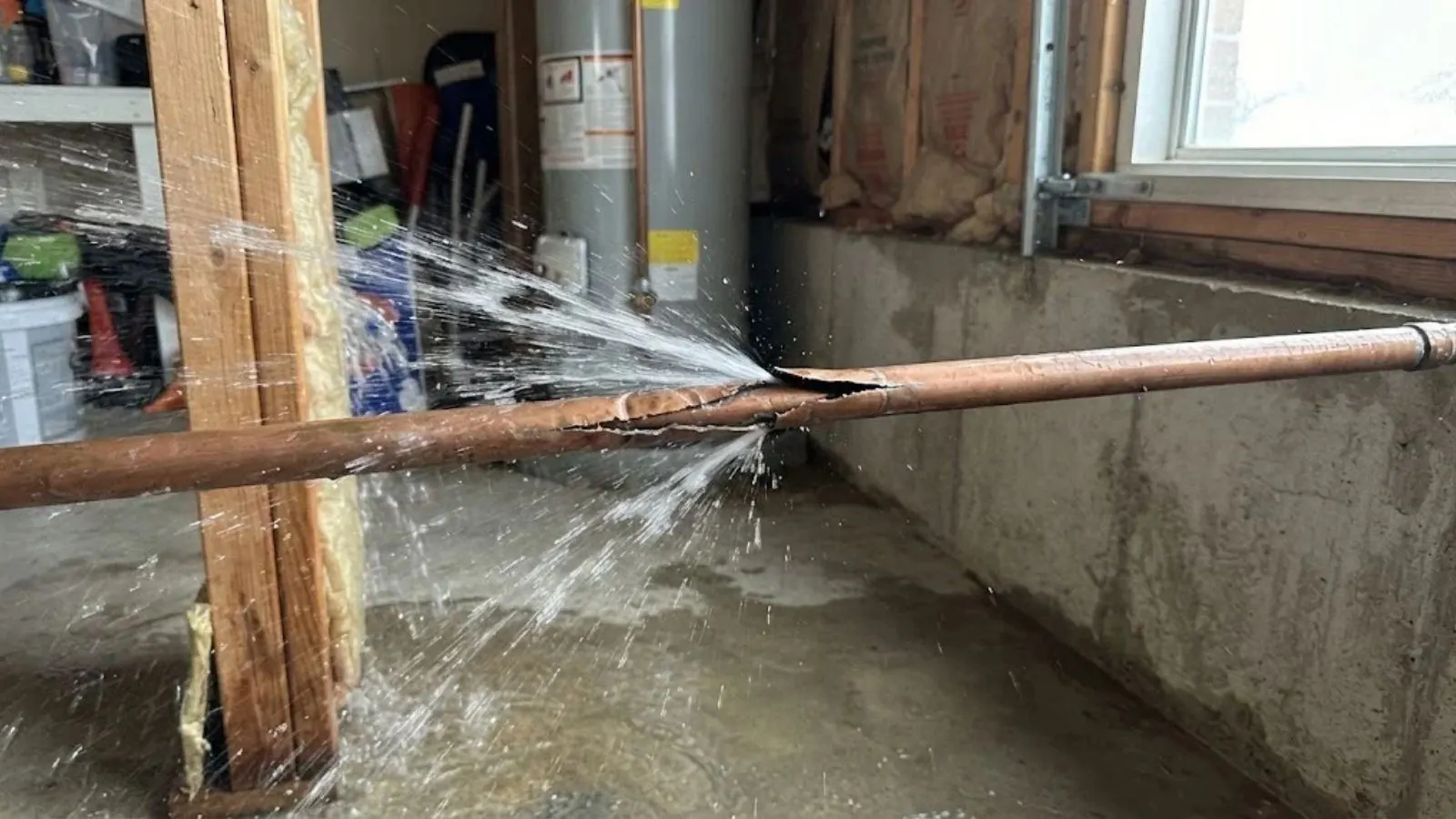 Split copper pipe spraying water in a basement beside a water heater